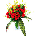 20 red roses arranged in a clear glass vase, gathe...